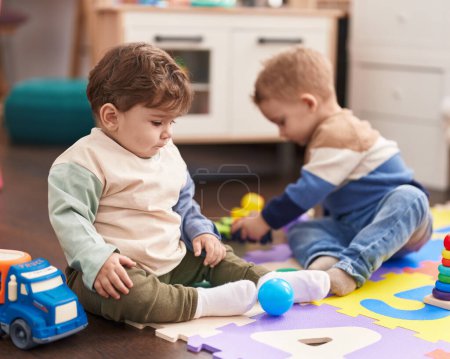 Foto de Dos niños sentados en el suelo jugando con juguetes en el jardín de infantes - Imagen libre de derechos