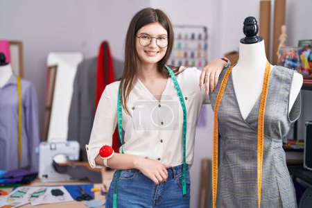Téléchargez les photos : Jeune femme caucasienne tailleur souriant confiant penché sur mannequin au magasin de tailleur - en image libre de droit