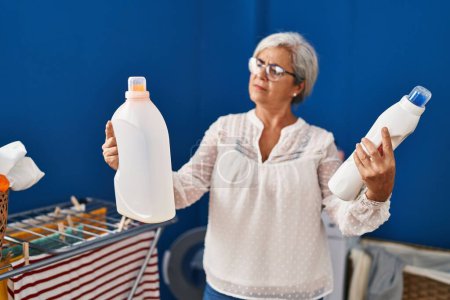 Téléchargez les photos : Middle age woman choosing detergent at laundry room - en image libre de droit