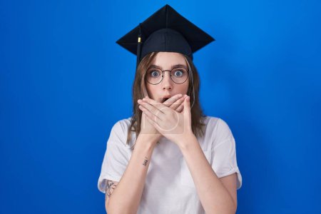 Foto de Blonde caucasian woman wearing graduation cap shocked covering mouth with hands for mistake. secret concept. - Imagen libre de derechos