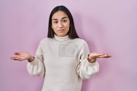 Foto de Young south asian woman standing over pink background clueless and confused with open arms, no idea concept. - Imagen libre de derechos