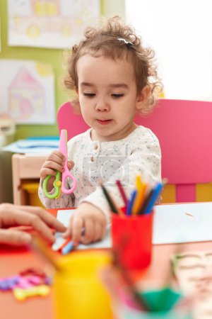 Photo for Adorable hispanic toddler student sitting on table drawing on paper at kindergarten - Royalty Free Image