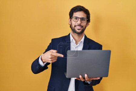 Foto de Hombre latino guapo trabajando usando computadora portátil mirando confiado con sonrisa en la cara, apuntándose con los dedos orgullosos y felices. - Imagen libre de derechos