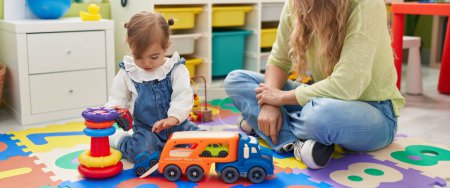 Photo for Teacher and toddler playing with cars toy sitting on floor at kindergarten - Royalty Free Image