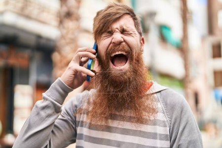 Téléchargez les photos : Jeune rousse homme parlant sur le smartphone criant à la rue - en image libre de droit