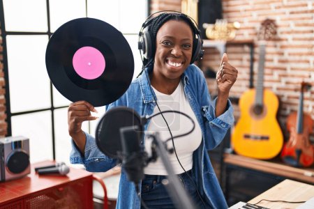 Photo for Beautiful black woman holding vinyl record at music studio screaming proud, celebrating victory and success very excited with raised arm - Royalty Free Image