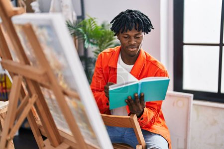 Téléchargez les photos : African american man artist reading book drawing at art studio - en image libre de droit