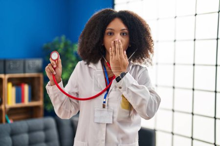 Photo for Young african american doctor woman wearing doctor uniform and stethoscope covering mouth with hand, shocked and afraid for mistake. surprised expression - Royalty Free Image