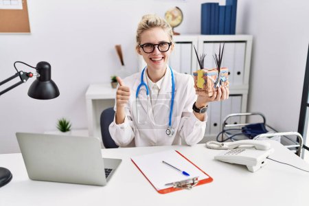 Photo for Young doctor woman holding model of human anatomical skin and hair at the clinic smiling happy and positive, thumb up doing excellent and approval sign - Royalty Free Image