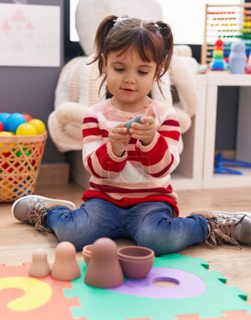 Foto de Adorable chica hispana jugando con juguetes sentados en el suelo en el jardín de infantes - Imagen libre de derechos