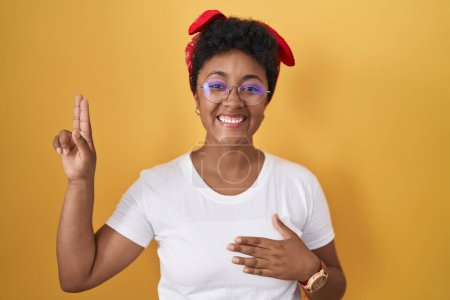 Téléchargez les photos : Young african american woman standing over yellow background smiling swearing with hand on chest and fingers up, making a loyalty promise oath - en image libre de droit