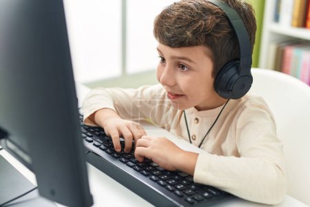 Téléchargez les photos : Adorable élève hispanique garçon en utilisant l'ordinateur assis sur la table en classe - en image libre de droit