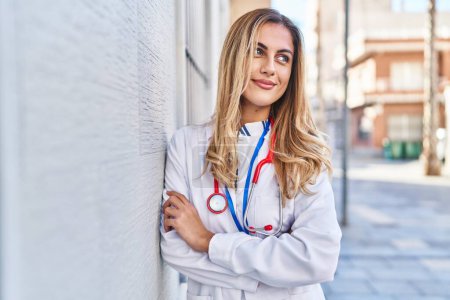 Téléchargez les photos : Jeune femme blonde portant l'uniforme de médecin debout à l'hôpital - en image libre de droit