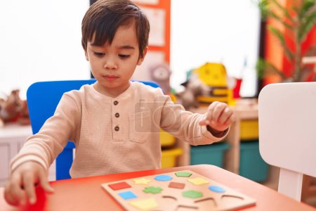 Photo for Adorable hispanic boy playing with maths puzzle game sitting on table at kindergarten - Royalty Free Image