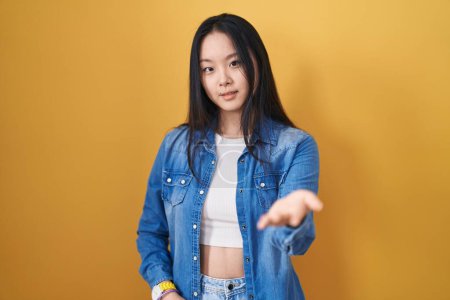 Téléchargez les photos : Young asian woman standing over yellow background smiling cheerful offering palm hand giving assistance and acceptance. - en image libre de droit