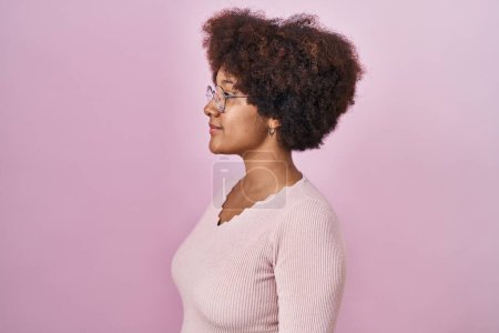 Téléchargez les photos : Young african american woman standing over pink background looking to side, relax profile pose with natural face and confident smile. - en image libre de droit