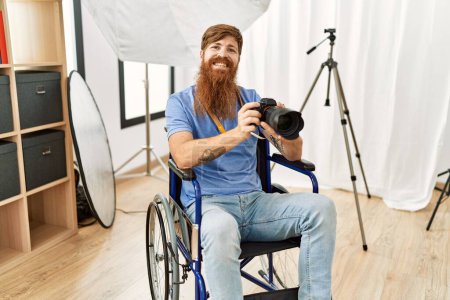 Foto de Joven fotógrafo pelirrojo sentado en silla de ruedas usando cámara profesional en la clínica - Imagen libre de derechos