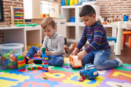 Foto de Dos niños jugando con bloques de construcción y juguete de camión sentado en el suelo en el jardín de infantes - Imagen libre de derechos