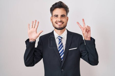 Foto de Young hispanic man with tattoos wearing business suit and tie showing and pointing up with fingers number seven while smiling confident and happy. - Imagen libre de derechos