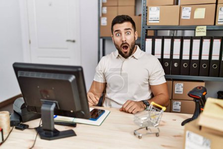 Photo for Handsome hispanic man working at small business commerce in shock face, looking skeptical and sarcastic, surprised with open mouth - Royalty Free Image
