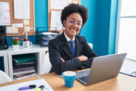 Téléchargez les photos : Femme afro-américaine travailleur d'affaires en utilisant un ordinateur portable assis avec les bras croisés geste au bureau - en image libre de droit