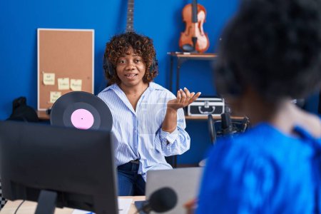 Téléchargez les photos : African american women musicians holding vinyl disc speaking at music studio - en image libre de droit