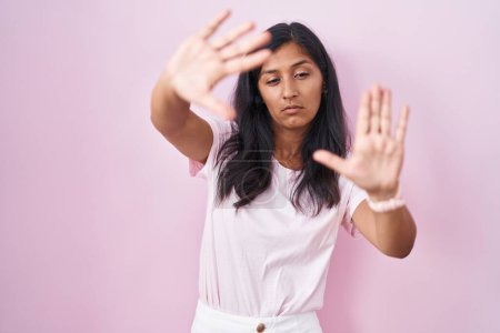 Photo for Young hispanic woman standing over pink background doing frame using hands palms and fingers, camera perspective - Royalty Free Image