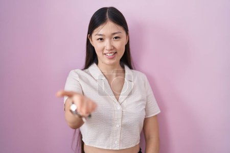 Foto de Chinese young woman standing over pink background smiling cheerful offering palm hand giving assistance and acceptance. - Imagen libre de derechos