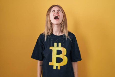 Photo for Blonde caucasian woman wearing bitcoin t shirt angry and mad screaming frustrated and furious, shouting with anger. rage and aggressive concept. - Royalty Free Image