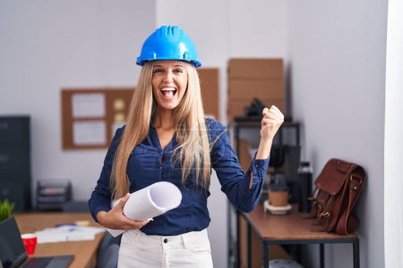 Photo for Young woman wearing architect hardhat screaming proud, celebrating victory and success very excited with raised arms - Royalty Free Image
