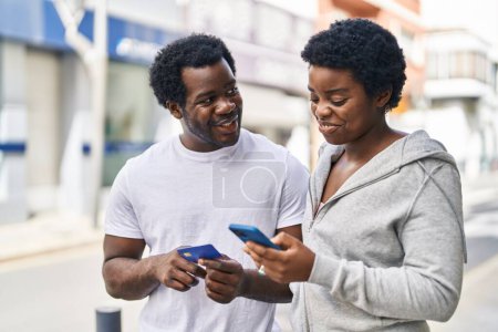 Foto de Africano americano hombre y mujer pareja usando teléfono inteligente y tarjeta de crédito en la calle - Imagen libre de derechos