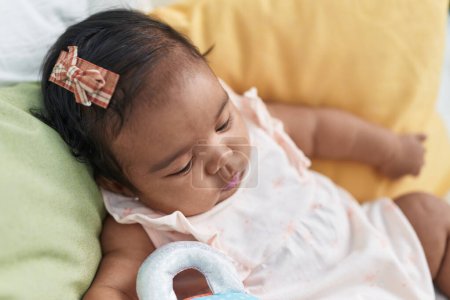 Téléchargez les photos : Bébé afro-américain assis sur le lit avec une expression détendue dans la chambre - en image libre de droit