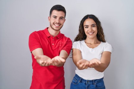 Téléchargez les photos : Jeune couple hispanique debout sur fond isolé souriant avec les mains paumes ensemble recevant ou donnant geste. maintien et protection - en image libre de droit