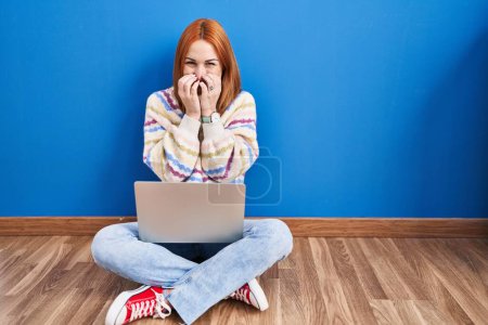 Foto de Mujer joven usando el ordenador portátil en casa sentado en el suelo riendo y riéndose avergonzado cubriendo la boca con las manos, chismes y concepto de escándalo - Imagen libre de derechos