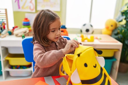 Photo for Adorable hispanic girl student closing backpack sitting on table at kindergarten - Royalty Free Image