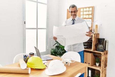 Photo for Middle age grey-haired man architect looking house plans at office - Royalty Free Image