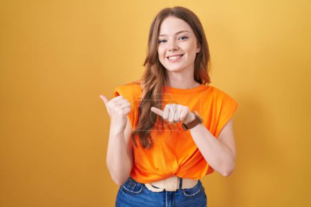 Photo for Caucasian woman standing over yellow background pointing to the back behind with hand and thumbs up, smiling confident - Royalty Free Image