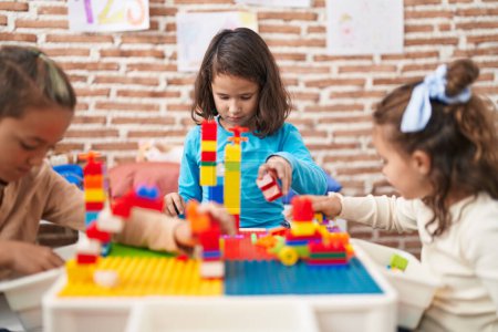 Téléchargez les photos : Group of kids playing with construction blocks sitting on table at kindergarten - en image libre de droit