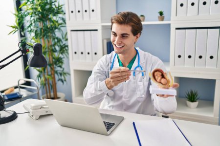 Foto de Hombre joven caucásico médico sosteniendo modelo anatómico del útero con el feto hablando en la clínica - Imagen libre de derechos