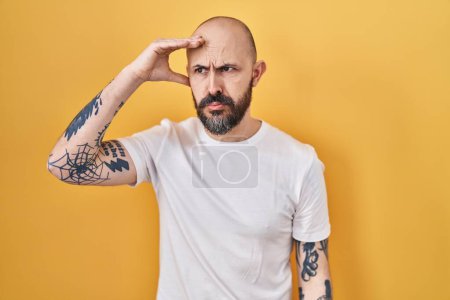 Photo for Young hispanic man with tattoos standing over yellow background worried and stressed about a problem with hand on forehead, nervous and anxious for crisis - Royalty Free Image