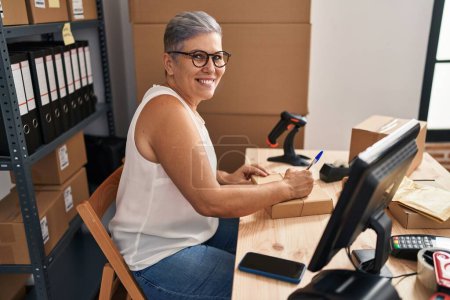 Téléchargez les photos : Femme d'âge moyen ecommerce travailleur d'affaires écrivant sur le paquet au bureau - en image libre de droit