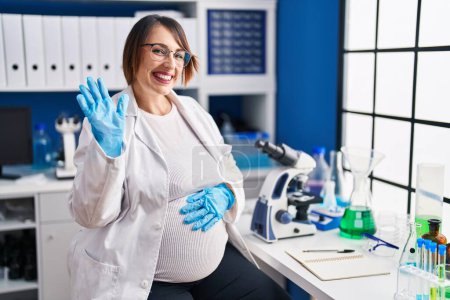 Téléchargez les photos : Femme enceinte travaillant au laboratoire scientifique renonçant à dire bonjour heureux et souriant, geste de bienvenue amical - en image libre de droit