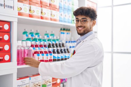 Photo for Young arab man pharmacist smiling confident organizing shelving at pharmacy - Royalty Free Image