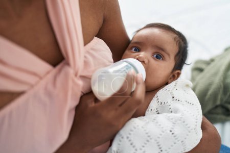 Foto de African american baby sucking feeding bottle at bedroom - Imagen libre de derechos