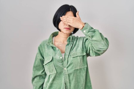 Téléchargez les photos : Young asian woman standing over white background covering eyes with hand, looking serious and sad. sightless, hiding and rejection concept - en image libre de droit