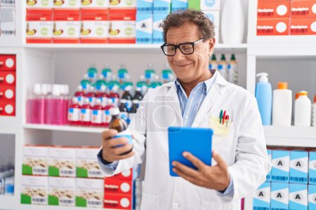 Téléchargez les photos : Middle age man pharmacist using touchpad holding medicine bottle at pharmacy - en image libre de droit