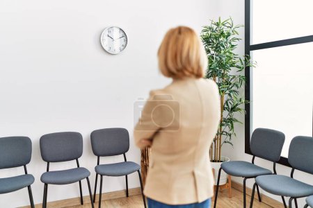 Téléchargez les photos : Middle age blonde woman on back view looking clock at waiting room - en image libre de droit
