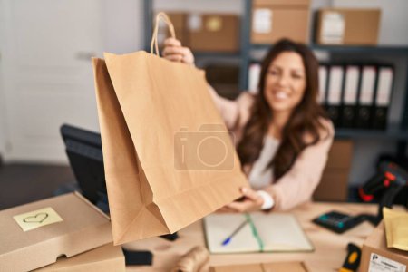 Photo for Young hispanic woman ecommerce business worker holding order paper bag at office - Royalty Free Image