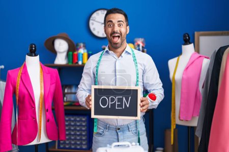 Photo for Hispanic man with beard working as dressmaker at atelier celebrating crazy and amazed for success with open eyes screaming excited. - Royalty Free Image