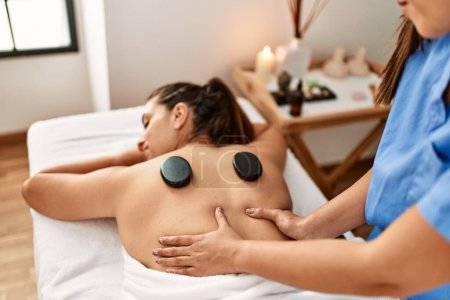 Photo for Two women therapist and patient having back massage session using black stones at beauty center - Royalty Free Image